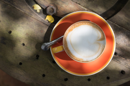 hot cappuccino coffee in orange cup on wooden tableの写真素材