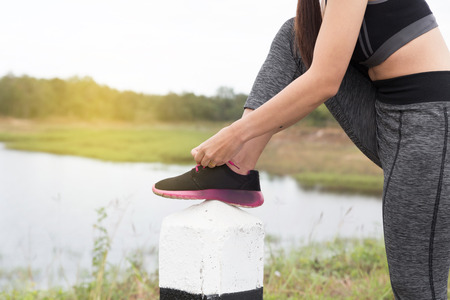 woman tying shoe laces. Female sport fitness runner getting ready for jogging outdoors on road in parkの写真素材