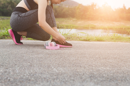 woman tying shoe laces. Female sport fitness runner getting ready for jogging outdoors on road in parkの写真素材