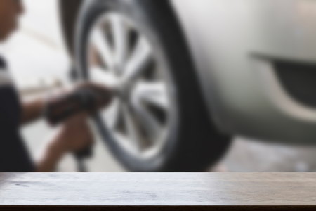 mechanic hands with tool, changing tyre of car in garage (blur image) with selected focus empty wood table for display your productの写真素材