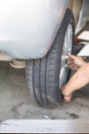 mechanic changing tyre of car in garage (blur image) with selected focus empty wood table for display your productの写真素材