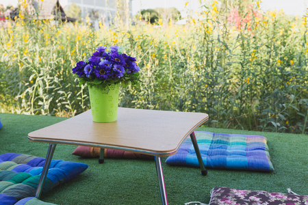 Patio outdoor deck with colorful cushion and flower decoration on table, exterior of home with yellow flower fieldの写真素材