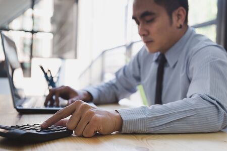 Businessman Analyzing financial data on computer and counting on calculator in officeの写真素材