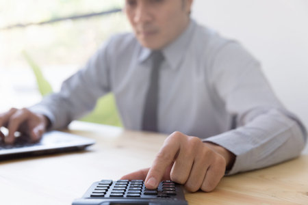Businessman Analyzing financial data on computer and counting on calculator in office