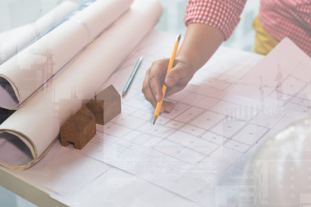 Architect or engineer working on blueprint at workplace - architectural project, Construction concept, double exposure with crane and building under constructionの写真素材