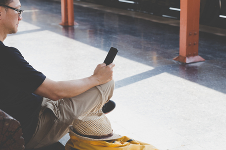 Traveler man with a backpack sitting and waiting for train on the station. Outdoor adventure travel by train conceptの写真素材