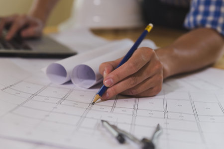 Architect or engineer working on blueprint and laptop at workplace - architectural project,...