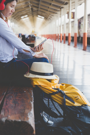 Traveler girl with a backpack sitting and waiting for train on the station. Outdoor adventure travel by train conceptの写真素材