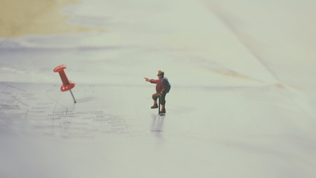 Selective focus of Miniature figurine of lonely young traveler with backpack walking on big map with red pinの写真素材