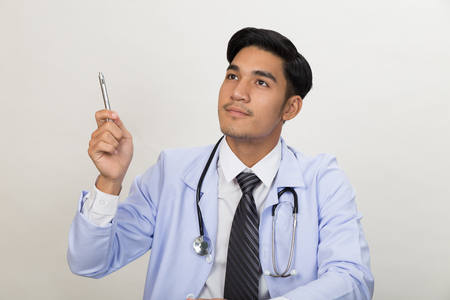 handsome thoughtful young male doctor thinking about treatment and pointing pen up while he has an ideaの写真素材