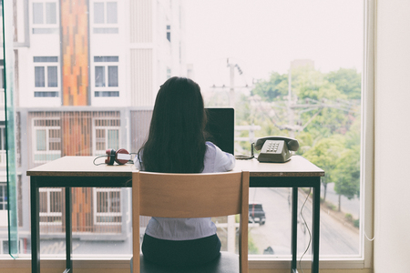 happy asian young girl sitting at table learning, studying online with headphones, laptop computer at home - people, technology and education conceptの写真素材