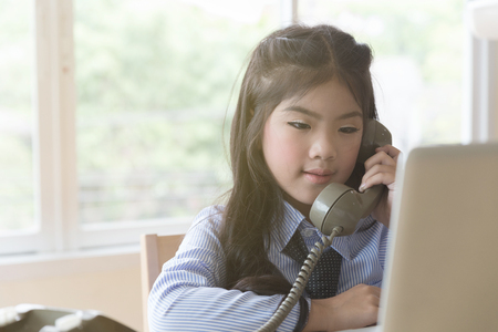 young beautiful casual girl making call, using telephone, talking on phone while sitting at modern workplace with laptop computerの写真素材