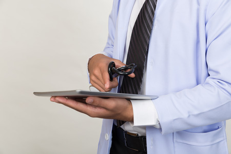 Male doctor hand holding stethoscope and working with modern digital tablet or touchpad at workplace - Medical technology concept.の写真素材