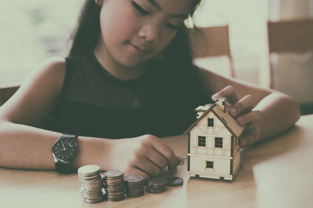 asian girl hold little house with money pile stack - money saving education conceptの写真素材