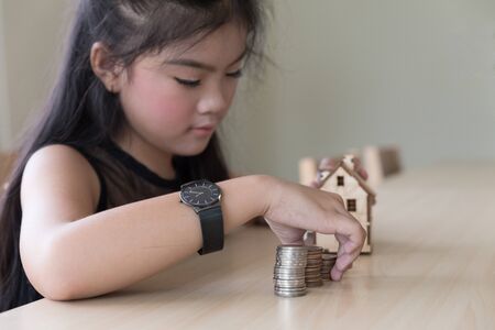 asian girl hand putting coins to money pile stack with little house - money saving education conceptの写真素材