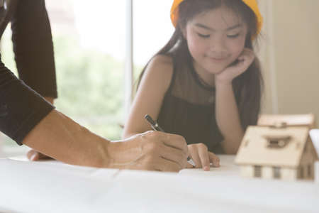 asian little girl in protective construction helmet studying, learning engineering and architecture on blueprint with guidance of her teacher - childhood education conceptの写真素材