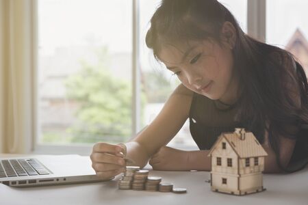 asian girl hand putting coins to money pile stack with little house - money saving education conceptの写真素材