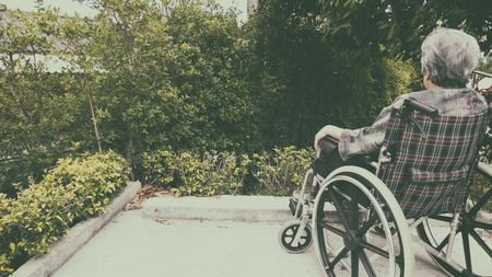 Old woman sitting alone in a wheelchair out in the garden at homeの写真素材