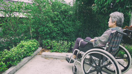 Old woman sitting alone in a wheelchair out in the garden at homeの写真素材