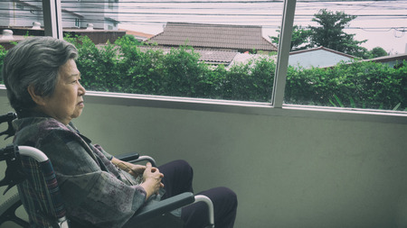 lonely senior woman looking through window in building - age, loneliness and people conceptの写真素材