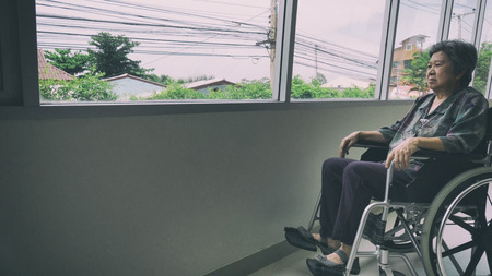 lonely senior woman looking through window in building - age, loneliness and people conceptの写真素材
