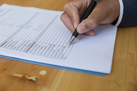 man 's hand fill out reverse mortgage loan application on a clipboard. A form to be filled by a homeowner who want to turn their asset into cash.の写真素材