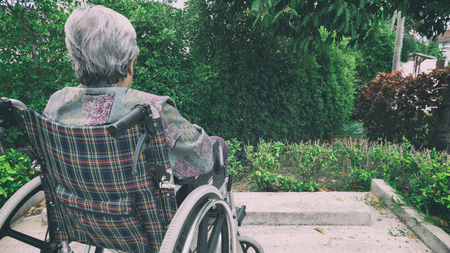 Old woman sitting alone in a wheelchair out in the garden at homeの写真素材