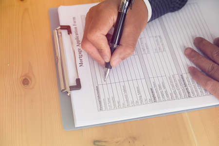 man 's hand fill out mortgage loan application on a clipboard. A form to be filled by a homeowner who want to turn their asset into cash.の写真素材