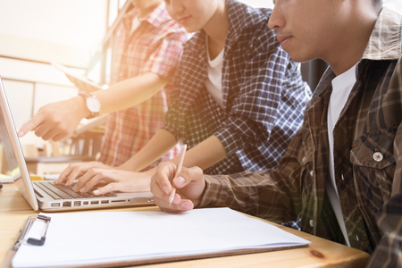 young university students studying with computer in cafe. Group of people in campus library. College teenager using laptop at table. Group study for school assignment.の写真素材