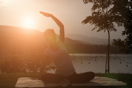 silhouette of female asian pregnant woman practicing yoga on green grass in public park. concept of prenatal exercise, maternity, fitness, healthy lifestyle and relaxation.の写真素材