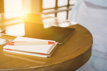 pen, notepad and digital tablet on wood table near window in cafe coffee shopの写真素材