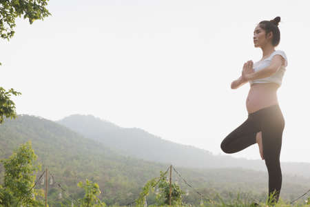 female asian pregnant woman practicing yoga on green grass in public park. concept of prenatal exercise, maternity, fitness, healthy lifestyle and relaxation.の写真素材
