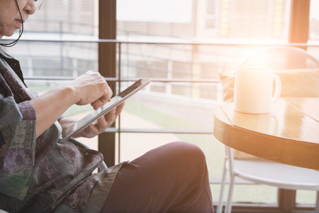 asian senior woman sitting and resting in cafe coffee shop near window using digital tablet...