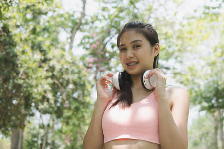 young beautiful asian fitness athlete woman with white headphones preparing for a jogging in summer park.の写真素材