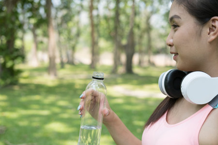 young beautiful asian fitness athlete woman holding drinking water after work out exercising at...