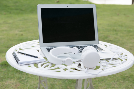 Laptop computer and headphone on white table in park.  freelance or remote work conceptの写真素材