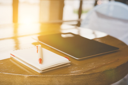 pen, notepad and digital tablet on wood table near window in cafe coffee shopの写真素材