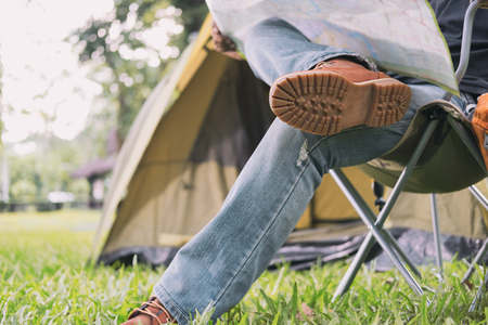 man tourist sitting on chair and reading map in front of tent at camping site in forest. Outdoor activity in summer. Adventure traveling in national park. leisure, vacation, relaxation conceptの写真素材