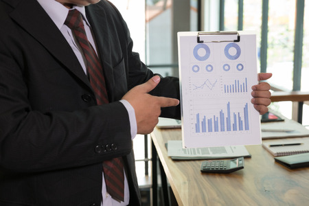 Businessman pointing at analytic financial accounting market chart and graph report summary, business statistics performance conceptの写真素材