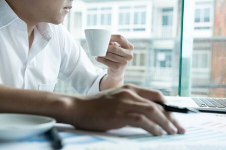young male graphic designer working with computer at modern office. businessman drink coffee in the morning. architect with color swatch sample catalog. business, technology, design and people conceptの写真素材