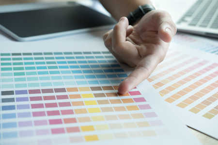 young male graphic designer working with computer, color swatch sample colour catalog. creative man using digital tablet at modern office.  Architectural drawing with work tools and accessories. business, technology, design and people conceptの写真素材