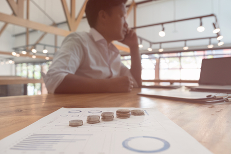 Businessman using smart phone with currency money coin and accounting graph and chart on table at office. growth of financial income from investment.の写真素材