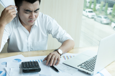 Man calculate domestic bills at home. Businessman using calculator at modern office. Young male checking balance and costs.  Start up counting finance. Business people doing paperwork for paying taxes. stressful, frustrated, upset conceptの写真素材