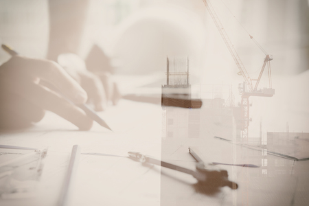 young architect working on real estate project at workplace. Male engineer hand working with living house blueprint at office. Business, people, construction and building concept double exposure with craneの写真素材