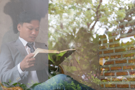 Young asian businessman wearing white shirt and gray suit reading book in cafe. view through windowの写真素材