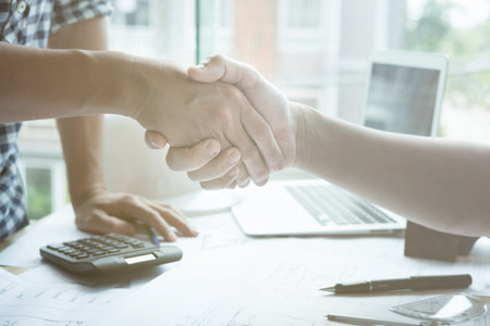 young architect and customer shaking hands at workplace. Engineer handshaking with partner for...