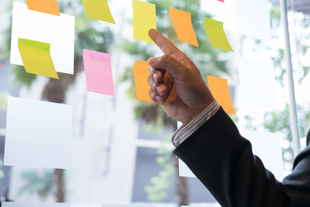 Businessman look at the adhesive notes on glass wall in meeting room. Sticky note paper reminder schedule for discussing idea in office. business, teamwork, brainstorming conceptの写真素材