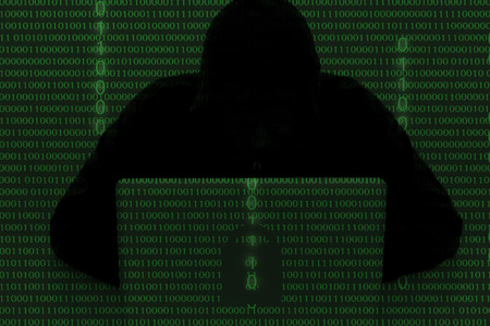 computer hacker wearing a hooded top using laptop in the dark. The man breaks the access to steal information and infect computers and systems. hacking, network security, identity theft and internet crime double exposure with 01 code binary numberの写真素材
