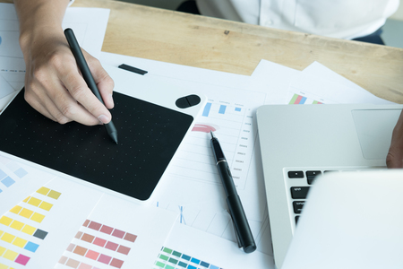 young male graphic designer working with computer and color swatch. creative man using stylus pen and digital tablet at modern office. Architect using work tools and sample colour catalog. business, technology, design and people conceptの写真素材