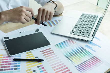 young male graphic designer working with computer and color swatch. creative man using stylus pen and digital tablet at modern office. Architect using work tools and sample colour catalog. business, technology, design and people conceptの写真素材